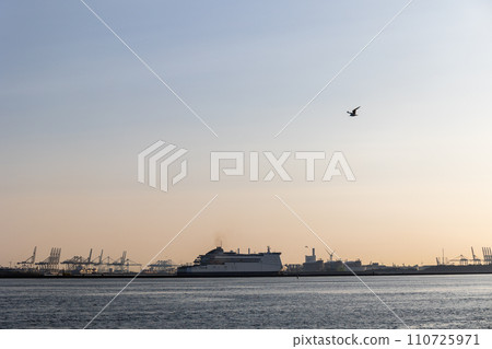 Ships float across the North Sea. Windmills in the background. Sea port in the Netherlands. A lot of cranes for loading goods. Different ships and barges. 110725971
