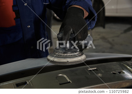 A man at a car maintenance station cleans the car part with an instrument. Preparation of car parts for painting. Car repair at the station. Car service. A man at a car maintenance station cleans the car part with an instrument. Preparation of car parts for painting. Car repair at the station. Car service. 110725982