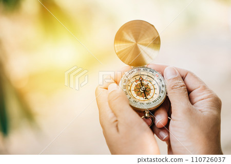 A close-up of a woman using a compass in the forest highlighting guidance and exploration. Her hand holds the compass in the midst of nature's beauty. A close-up of a woman using a compass in the forest highlighting guidance and exploration. Her hand holds the compass in the midst of nature's beauty. 110726037