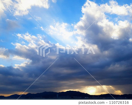 夕陽的光芒透過雲層和山巒的輪廓閃耀 夕陽的光芒透過雲層和山巒的輪廓閃耀 110726316