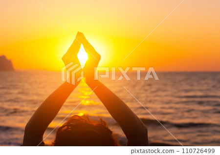 Woman's hands symbolizing prayer and gratitude. Mudra. Yoga concept. Silhouette of female hands on sun background. Beautiful scene Woman's hands symbolizing prayer and gratitude. Mudra. Yoga concept. Silhouette of female hands on sun background. Beautiful scene 110726499