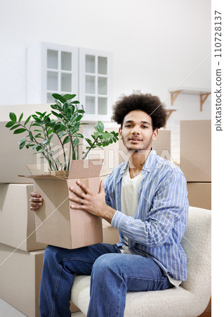 happy young African American man moves into new home. person is sitting among cardboard boxes  110728137