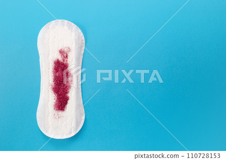 Feminine hygiene pad with red glitter on blue background. First menstrual period concept  110728153