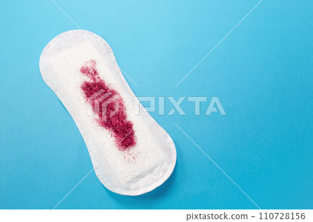 Feminine hygiene pad with red glitter on blue background. First menstrual period concept Feminine hygiene pad with red glitter on blue background. First menstrual period concept 110728156