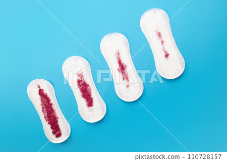 Feminine hygiene pads with red glitter on blue background. First menstrual period concept Feminine hygiene pads with red glitter on blue background. First menstrual period concept 110728157