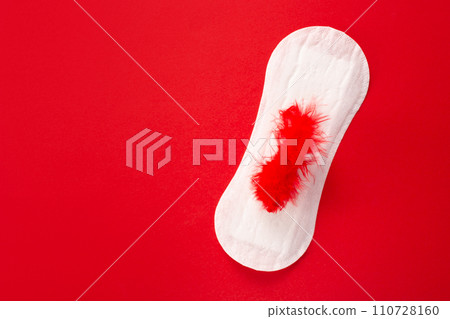 Feminine hygiene pad with red feather on menstrual pad on red background. First menstrual period concept. Copy space 110728160