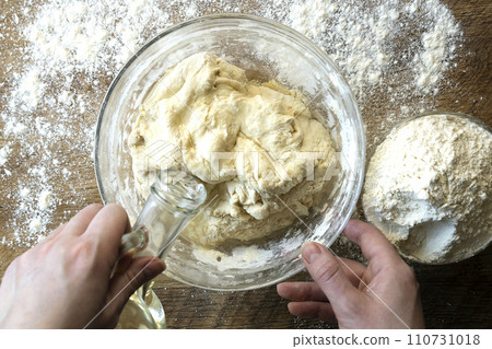 Top view of female hands adding oil to dough on flour background, bread baking concept. 110731018