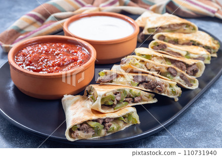Fajita quesadilla with pieces of beef steak, green bell pepper, onion and cheese, on a plate Fajita quesadilla with pieces of beef steak, green bell pepper, onion and cheese, on a plate 110731940
