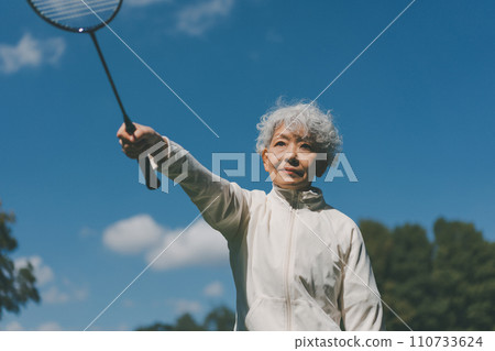 A woman in her 60s playing badminton outdoors A woman in her 60s playing badminton outdoors 110733624