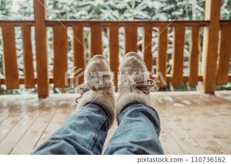 Woman legs in winter shoes - fur trendy boots on wooden balcony background. 110736162