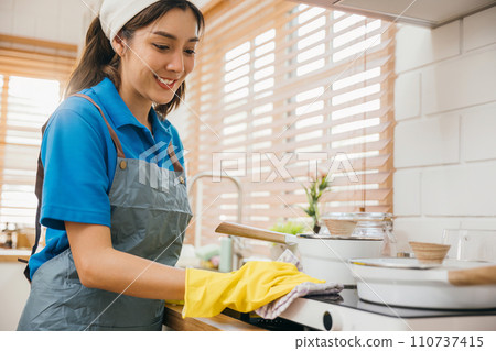Asian woman cleaning her kitchen gas stove hand in protective gloves. Wiping dust highlights hygiene and house care. Cleaner at work safety glove hygiene routine. Maid Cleaning housekeeping concept. Asian woman cleaning her kitchen gas stove hand in protective gloves. Wiping dust highlights hygiene and house care. Cleaner at work safety glove hygiene routine. Maid Cleaning housekeeping concept. 110737415