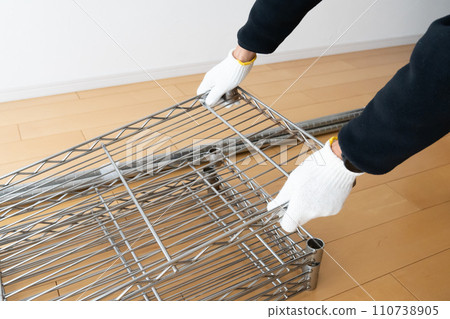 A hand wearing work gloves lifts a steel shelf A hand wearing work gloves lifts a steel shelf 110738905