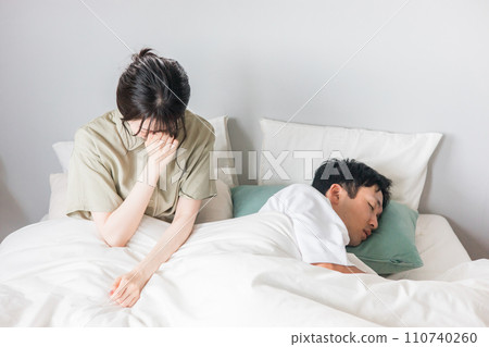 A woman suffering from lack of sleep and a man sleeping on the bed 110740260