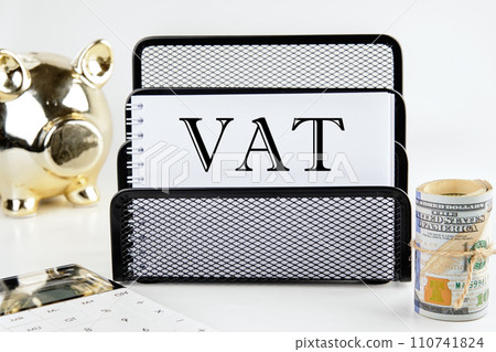 VAT text on a white piece of paper next to a piggy bank, a roll of money and a calculator on a white background 110741824