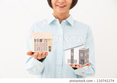 Middle-aged woman comparing two houses Middle-aged woman comparing two houses 110742274