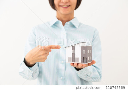Middle-aged woman pointing at a detached house model 110742369