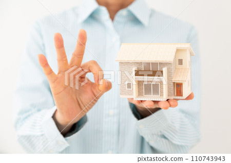 A middle-aged woman holding a model of a detached house and making a circle sign 110743943