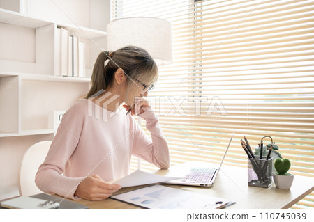 Work from home, Young woman analyzes data graphs on laptop and works intently in his personal office, Holding documents, Use your laptop for work and communication, Work from home, Young woman analyzes data graphs on laptop and works intently in his personal office, Holding documents, Use your laptop for work and communication, 110745039