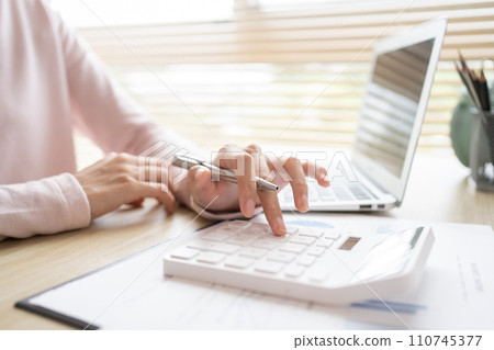 Close-up of hand pressing calculator to calculate income tax and company income in private office, Finance, Accounting, Tex, Statistical graphs of investing in real estate. 110745377