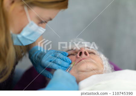 The cosmetologist performs small injections around the patient's mouth. The cosmetologist performs small injections around the patient's mouth. 110745390