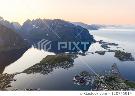 Aerial shot of Reine under midnight sun with mountain reflections and bridged islands Aerial shot of Reine under midnight sun with mountain reflections and bridged islands 110745914