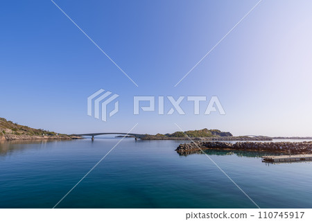 A bridge harmonizes with serene waters under a vast blue sky in Lofoten A bridge harmonizes with serene waters under a vast blue sky in Lofoten 110745917