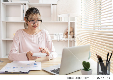 Young Businesswoman presses a calculator to calculate income tax and corporate income in a private office, Statistical graphs of investing in real estate, Finance, Accounting, Tex, Work for home. 110746075