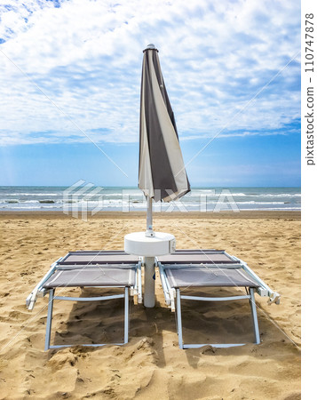 Two sunbeds and an umbrella closed in front of the sea 110747878