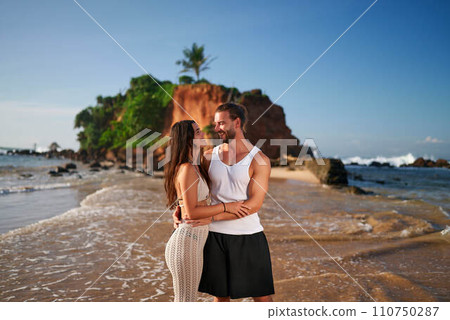 Romantic couple embraces on sandy beach at sunset. Man and woman enjoy tropical seaside, love and travel concept. Happy pair shares affectionate moment by sea, exotic vacation getaway. Romantic couple embraces on sandy beach at sunset. Man and woman enjoy tropical seaside, love and travel concept. Happy pair shares affectionate moment by sea, exotic vacation getaway. 110750287