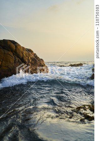 Ocean waves crash against rocks at sunrise. Seascape with splashing water near coastline. Marine natural beauty. Serene oceanic morning moment. Coastal sunrise with vivid water motion. 110750383