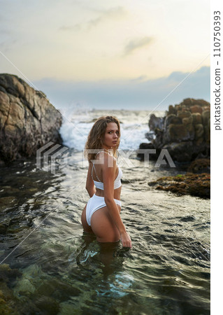 Woman in white swimsuit poses in sea water, fashion model explores tropical coastline, travel destination beauty shot. Woman in white swimsuit poses in sea water, fashion model explores tropical coastline, travel destination beauty shot. 110750393