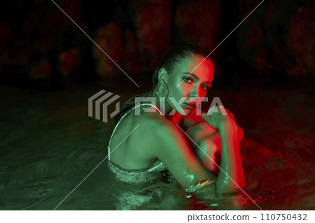Woman immersed in water at night, illuminated by red and green lights, portrays solitude and reflection, possible depression or post-trauma calmness. 110750432