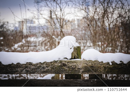 Big fluffy soft snowdrift on a wooden fence on snowy winter day with visible trees and modern buildings on the background Big fluffy soft snowdrift on a wooden fence on snowy winter day with visible trees and modern buildings on the background 110751644