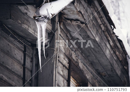 Steel broken drainpipe with icicles hanging on gray building roof corner on winter dull day 110751793