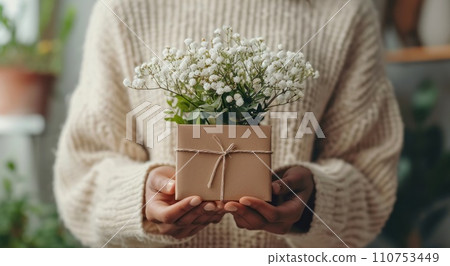 a woman's hands holding a brown box with flowers in it 110753449