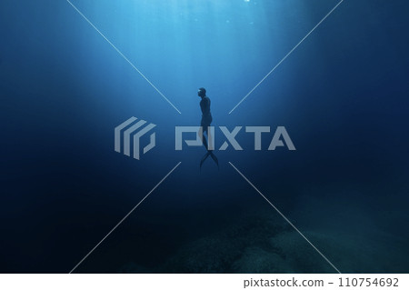Freediver Swimming in Deep Sea With Sunrays. Young Man DIver Eploring Sea Life. 110754692
