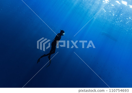 Freediver Swimming in Deep Sea With Sunrays. Young Man DIver Eploring Sea Life. Freediver Swimming in Deep Sea With Sunrays. Young Man DIver Eploring Sea Life. 110754693