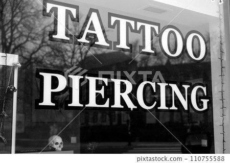 Closeup of tattoo piercing signage on the window of tattooing store in the street 110755588