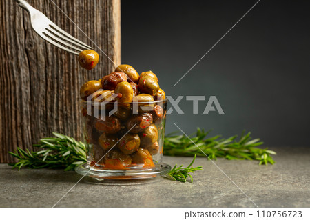 Spicy olives in a glass bowl on a stone table. 110756723