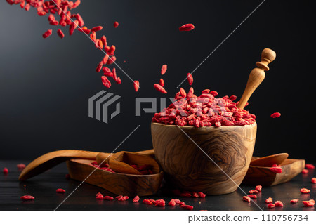 Dried goji berries in wooden bowl on a black background. Dried goji berries in wooden bowl on a black background. 110756734