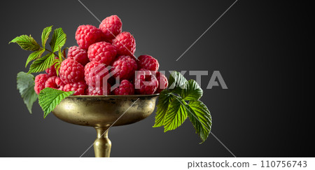 Fresh raspberries with leaves in an old brass dish. 110756743