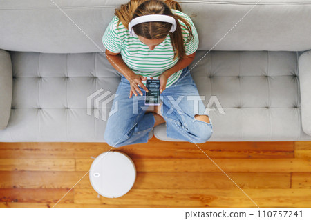 Woman Controlling Smart Vacuum Cleaner with Smartphone Woman Controlling Smart Vacuum Cleaner with Smartphone 110757241