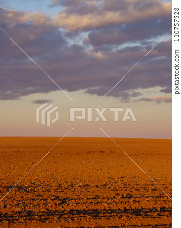 A vast barren land with scattered rocks under a cloudy sky. 110757528
