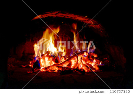 Flames dance above wood logs, casting a warm glow in the dark space. Flames dance above wood logs, casting a warm glow in the dark space. 110757530