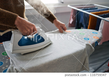 Hands of a mature man ironing laundry with steaming. Close-up. Clothes care concept. Hands of a mature man ironing laundry with steaming. Close-up. Clothes care concept. 110759347