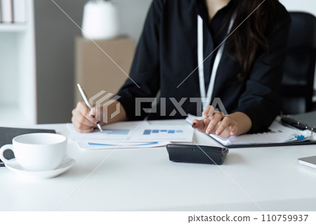 Businesswoman using a calculator to calculate numbers on a company's financial documents, she is analyzing historical financial data to plan how to grow the company. Financial concept Businesswoman using a calculator to calculate numbers on a company's financial documents, she is analyzing historical financial data to plan how to grow the company. Financial concept 110759937