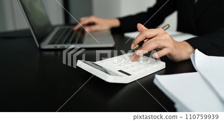 Businesswoman using a calculator to calculate numbers on a company's financial documents, she is analyzing historical financial data to plan how to grow the company. Financial concept Businesswoman using a calculator to calculate numbers on a company's financial documents, she is analyzing historical financial data to plan how to grow the company. Financial concept 110759939