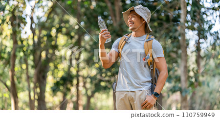 Young man backpacker traveling alone in forest. Attractive male traveler drinking water while walking in nature wood during holiday vacation trip 110759949