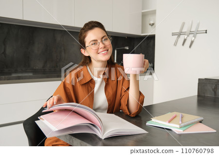 Portrait of beautiful student, woman in glasses reading and drinking coffee at home, studying and revising for lesson, doing homework 110760798