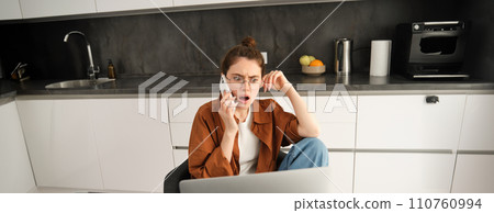 Portrait of woman with shocked face, receives concerning bad news over the phone conversation, sitting at home with laptop, working, talking to someone on telephone Portrait of woman with shocked face, receives concerning bad news over the phone conversation, sitting at home with laptop, working, talking to someone on telephone 110760994